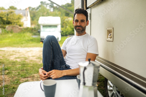 portrait of young man sitting next to his motor home drinking coffee. photo