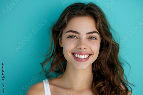 A woman with long brown hair is smiling against a blue background