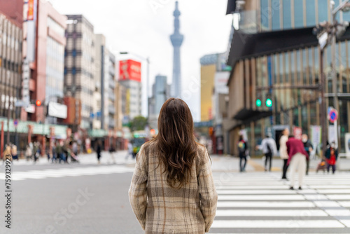 Happy Asian woman crossing street crosswalk with crowd of people during travel at Asakusa district, Tokyo, Japan. Attractive girl enjoy outdoor lifestyle travel in the city on holiday vacation.