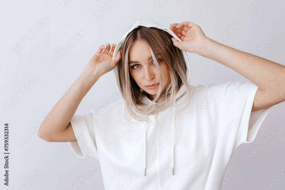 Charming young woman putting on white hoodie in studio Charming young woman putting on white hoodie in studio