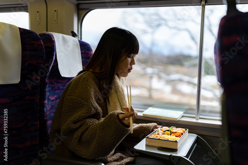 Asian woman eating traditional Japanese pork cutlet with rice Tonkatsu in lunch box bento during travel on train. Attractive girl travel Japan on railroad transportation on winter holiday vacation.