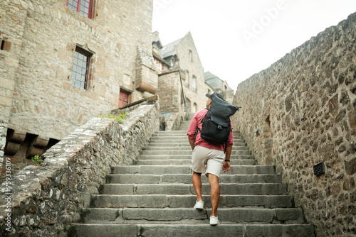 tourist man walking through mont saint michel with his backpack photo