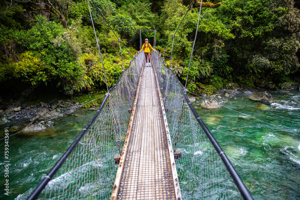 hiker crossing a rushing river in fiordland national park, new zealand south island, hiking trail to lake marian hiker crossing a rushing river in fiordland national park, new zealand south island, hiking trail to lake marian