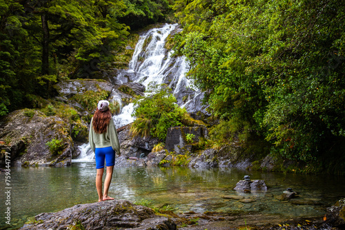 adventurous girl stands and looks at powerful Fantail Falls in Mount Aspiring National Park, Westland District, New Zealand, Haast River