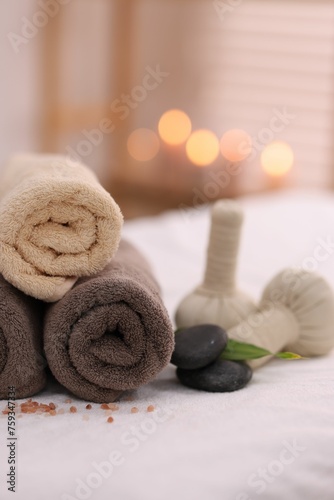 Spa stones, rolled towels and herbal bags on massage table indoors, closeup
