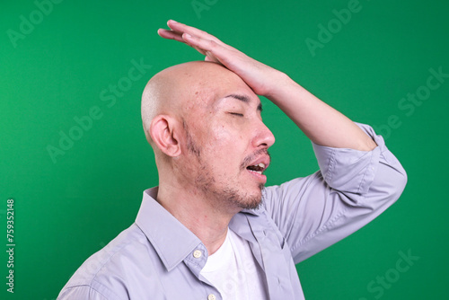 Forgetful Mature Man. Regrets wrong doing slapping hand on head having a duh moment isolated on green background.  photo