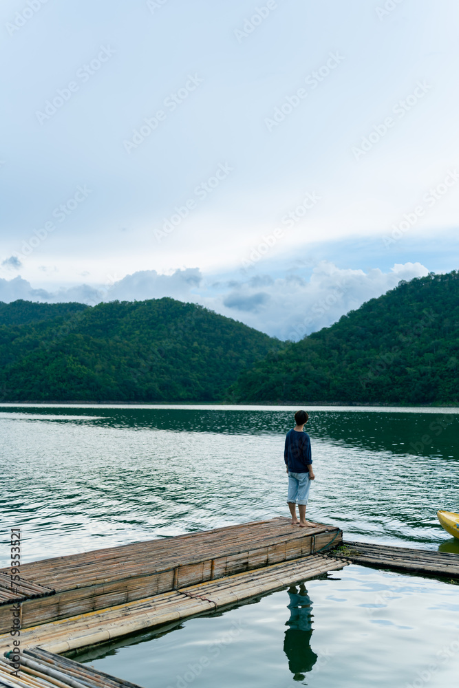 Young Asian man relax and enjoy outdoor lifestyle travel forest mountain on summer holiday vacation. Generation z guy relaxing on lake house balcony looking beautiful nature and breathing fresh air