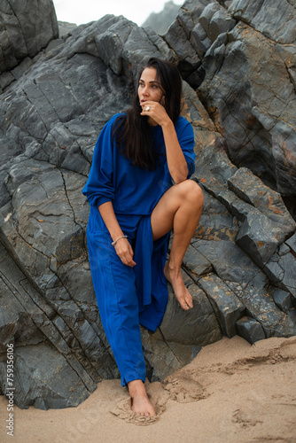 Woman in ultramarine blue clothes leaning on rock on the beach photo