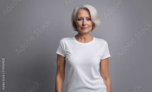 An elder female fashion model wearing a blank white t-shirt in front of a gray background. - Generative AI