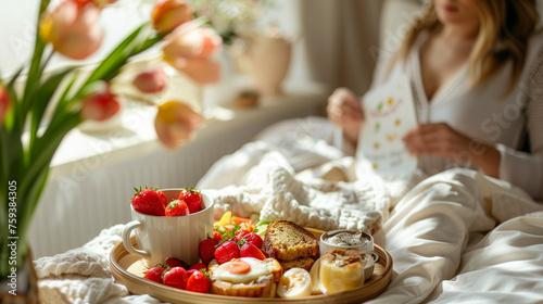 A stylish woman with long dark hair sits cross-legged on a plush bed, elegantly enjoying a tray of delicious food, Breakfast in bed Mother`s Day concept