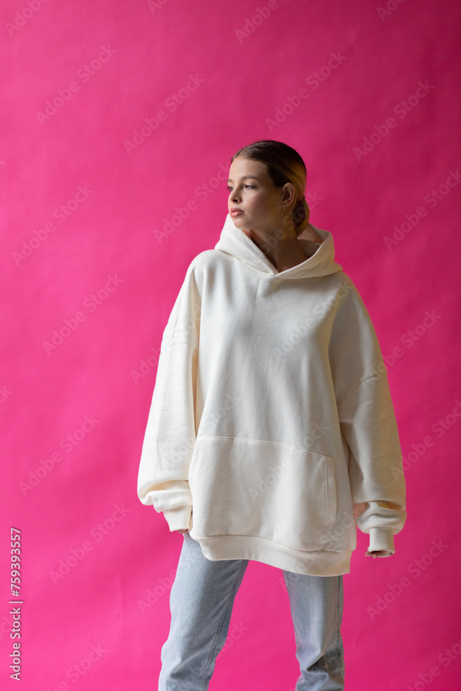 Beautiful blonde woman in a white hoodie and blue jeans posing on a pink background Beautiful blonde woman in a white hoodie and blue jeans posing on a pink background