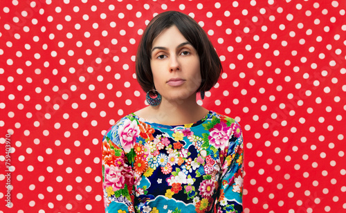 Portrait of a woman wearing a vibrant floral dress, set against a contrasting red polka dot background, showcasing bold patterns.
