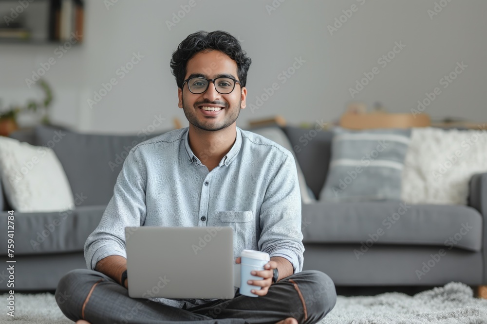 Smiling young man with glasses sitting on the floor with a laptop, Concept of remote work, digital lifestyle, and casual business Smiling young man with glasses sitting on the floor with a laptop, Concept of remote work, digital lifestyle, and casual business