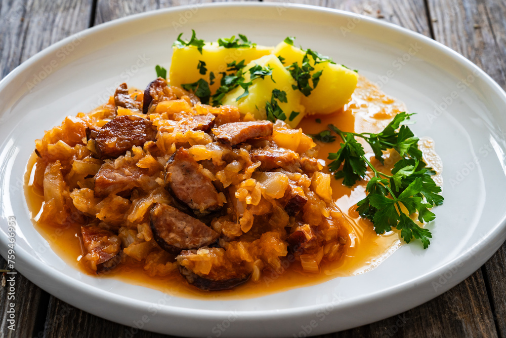 Bigos - cooked cabbage with sliced sausage and boiled potatoes on wooden table Bigos - cooked cabbage with sliced sausage and boiled potatoes on wooden table