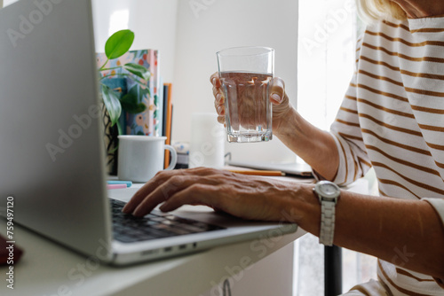 A senior woman by the computer with a glass of water photo