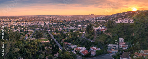 Aerial panorama of residential homes above city of Los Angeles cityscape shot from lush hiking trail in Hollywood Hills at sunset.