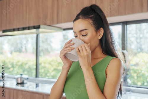 Tranquil Young Asian Woman Enjoying Hot Beverage in Modern Kitchen with Garden View