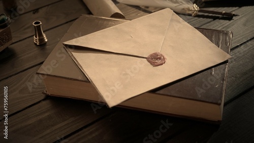 Shot of the table with old paper envelope. Vintage letter envelope laying on the old book sealed with wax stamp, feather quill and inkwell around.