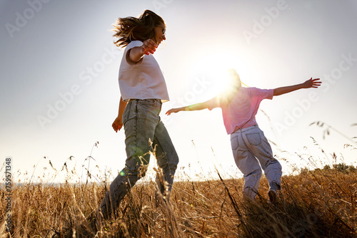 Two happy playful young girls runs in sunset field photo