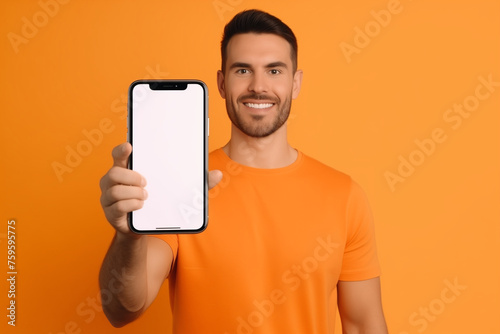 Mobile App Advertisement. Handsome Excited Man Showing Pointing At White Empty Smartphone Screen Posing Over Orange Studio Background, Smiling To Camera. Check This Out, Cellphone Display Mock Up