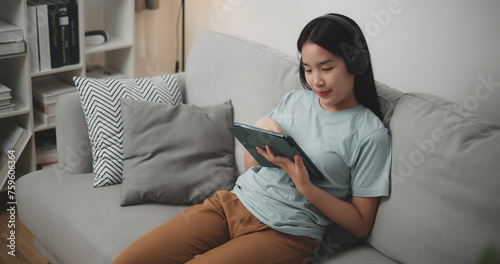 High angle view, Young asian woman wear wireless headphones sitting on sofa using digital tablet for online shopping cashless in living room at home