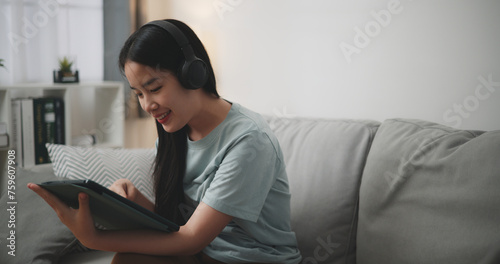 Selective focus, Happy young woman wear wireless headphones sitting on sofa using digital tablet for online shopping cashless in living room at home