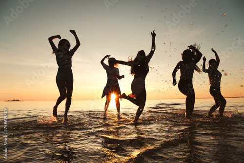 Silhouettes of happy girls are having fun and dancing at sunset lake beach