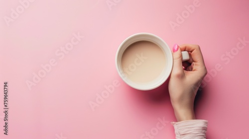 A female hand holding an empty mug on a pink background, captured in a flat l...