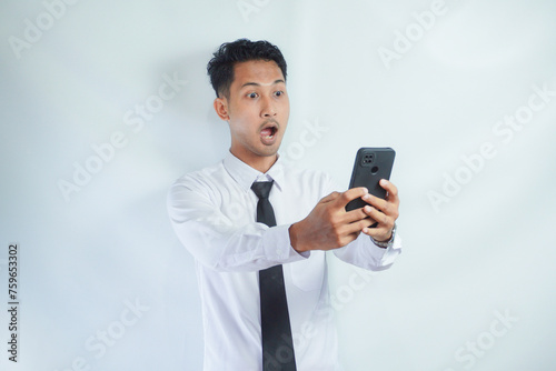 Adult Asian man looking to mobile phone that he hold with surprised expression photo