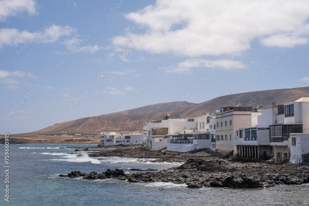Seascape. Arrieta village pier with typical white houses, mountains in the background. Turquoise Atlantic Ocean. Big white clouds. Village of Arrieta. Lanzarote, Canary Islands, Spain