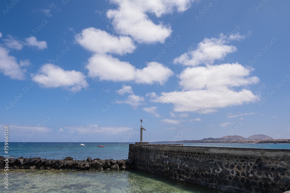 Seascape. Breakwater of the pier of the village of Arrieta with mountains in the background. Turquoise Atlantic Ocean. Big white clouds. Village of Arrieta. Lanzarote, Canary Islands, Spain