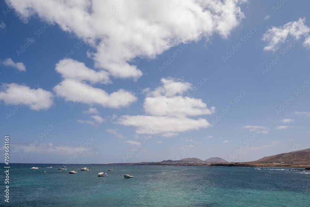 Seascape, calm sea. Group of boats anchored nearby. Mountains in the background. Turquoise Atlantic Ocean. Big white clouds. Village of Arrieta. Lanzarote, Canary Islands, Spain
