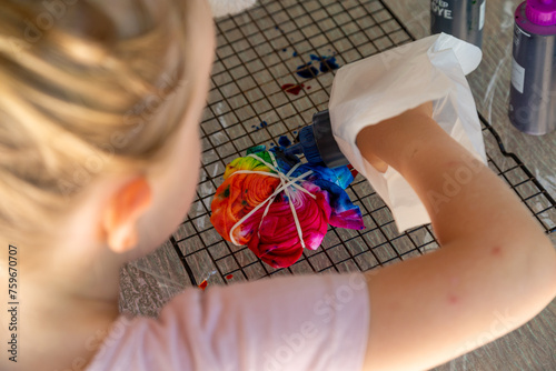 Young girl adds dye to colourful tie-dye on wire rack. photo