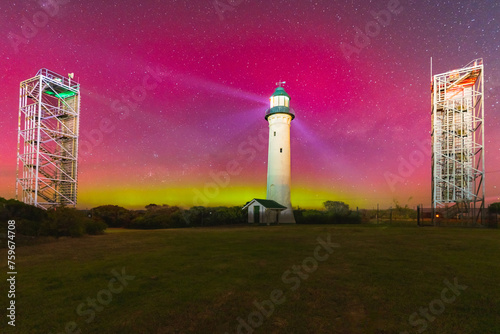 Aurora Australis filling the night sky over a tall lighthouse and nearby navigation towers photo