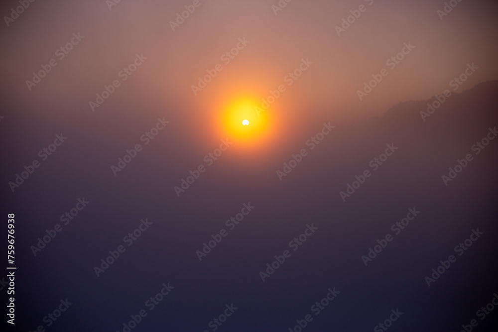 Selective focus sun with circles of orange light. Background image. Weak sunlight penetrates the thick fog on a mountaintop. The cold weather is about to receive gentle sunlight through the mist.