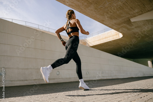 Fototapeta Naklejka Na Ścianę i Meble -  Back view of woman athlete in sportswear is running on buildings background. Active life concept