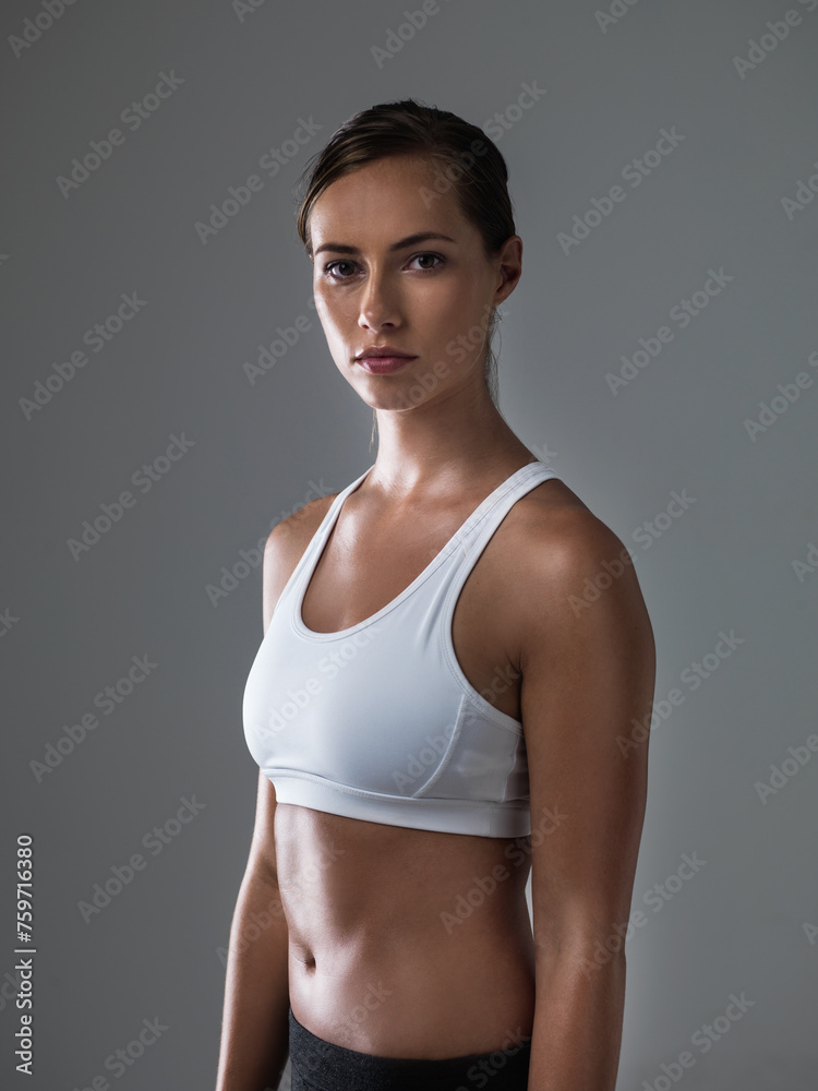 Fototapeta premium Woman, serious in portrait and confident for fitness, strong and determined with sweat from workout on grey background. Body, endurance and athlete for sports, exercise with pride and power in studio
