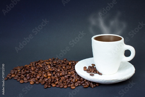 A pile of coffee beans, a white cup of coffee on a dark background. Front view.