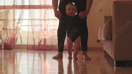 Cute baby trying to walk for the first time. Adorable infant holding his mother's hands while making his first steps. Slow-motion video of a Caucasian one-year-old boy walking for the first time. photo