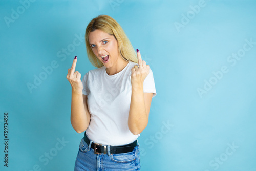 Young beautiful woman wearing casual t-shirt over isolated blue background showing middle finger doing fuck you bad expression, provocation and rude attitude. screaming excited photo