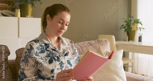 a woman is reading a book at home on a sofa in the beautiful daylight.