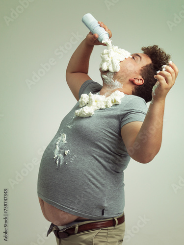 Plus size, eating and man with cream in studio for unhealthy, sugar and sweet snack or dessert. Messy, greedy and hungry plus size male person enjoying whipped dairy product by gray background.