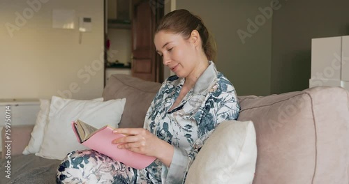 a woman is reading a book at home on a sofa in the beautiful daylight.