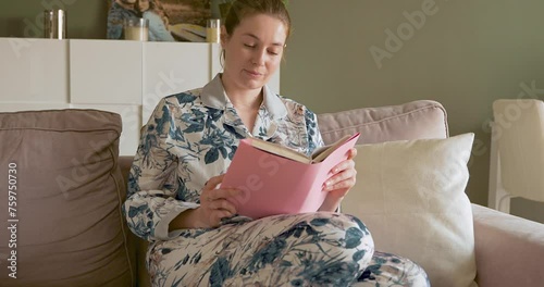 a woman is reading a book at home on a sofa in the beautiful daylight.
