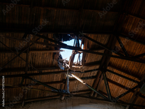 A war-torn interior with exposed beams, a roof damaged by a shell, and sunlight piercing through, the scene reflects conflict-induced destruction. High quality photo