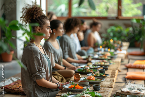 A support group practicing mindfulness eating to cultivate a healthy relationship with food. Yoga retreat center, prayer before meal.A group of people are sitting at a long table with plates of food