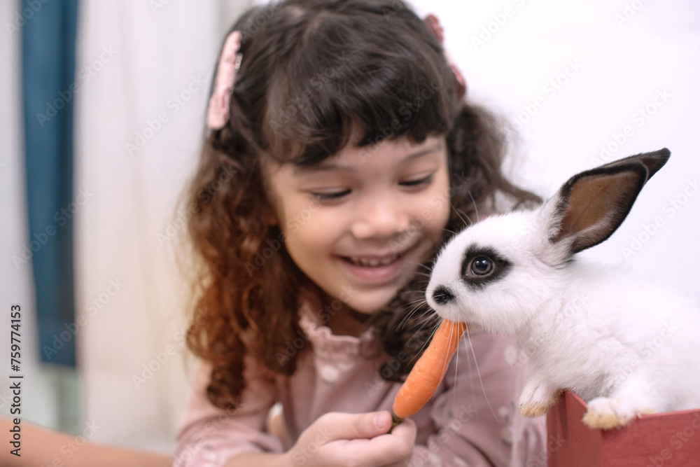 Cute little girl smiles happily with her rabbit pet, feeding a rabbit with carrots, selective focus, Easter symbol concept