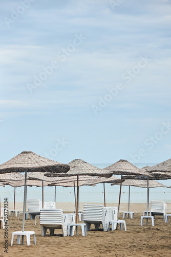 Sandy beach and beach umbrellas. White deck chairs in the form of stacks. Beach holidays