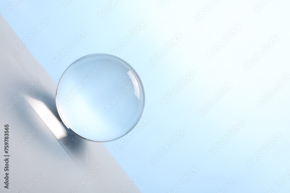 Transparent glass ball on table against light blue background. Space for text Transparent glass ball on table against light blue background. Space for text