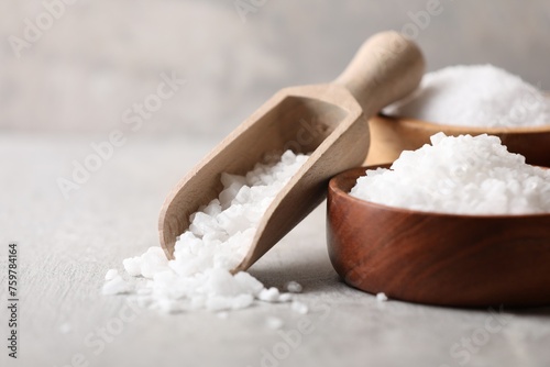 Natural salt in bowls and scoop on grey table, closeup